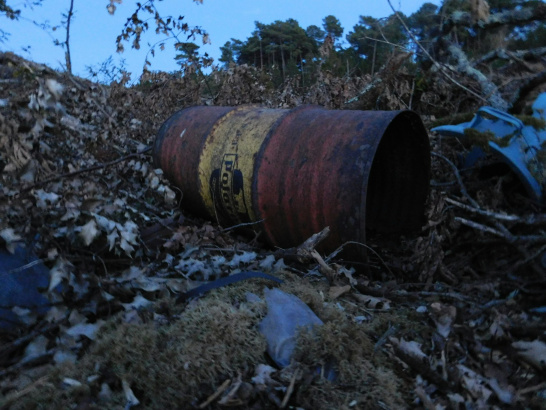 A rusty barrel sitting on a pile of leaves